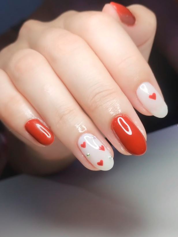 esmaltação em gel unha decorada com corações vermelhos e pequenas pedras de brilho